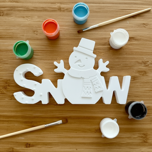 Snowman decoration piece with six small paint pots and two paintbrushes arranged around it on a wood background
