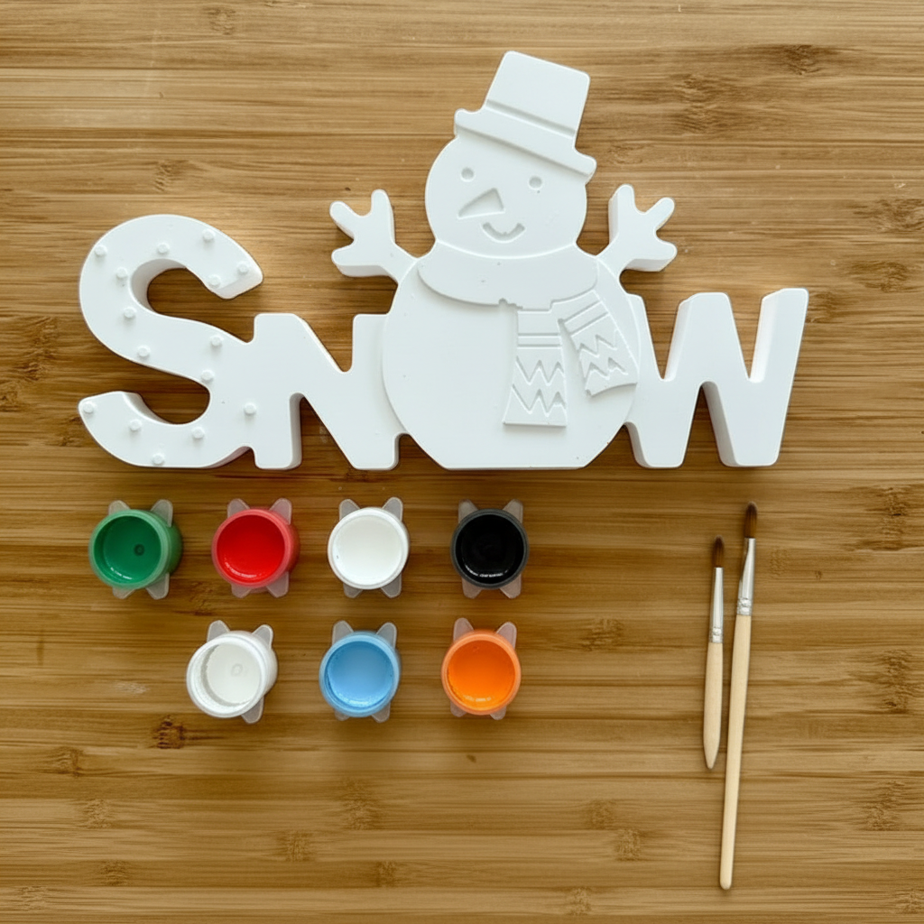 Unpainted snowman sign with six colorful paint pots and two paintbrushes on a wood background